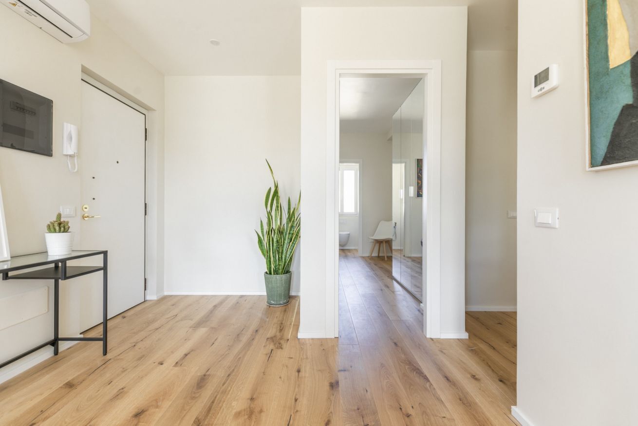 A hallway with wooden flooring, a potted plant, a small table with a plant, and a door.