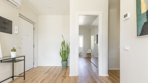 Un pasillo con piso de madera, una planta en maceta, una pequeña mesa con una planta y una puerta.