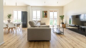 Una sala de estar moderna con sofá, mesa de comedor, sillas, televisor y un balcón con plantas.