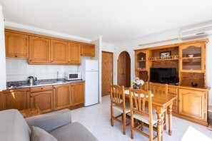 Una cuina compacta amb armaris de fusta, un microones, un frigorífic i una zona de menjador amb taula i cadires.