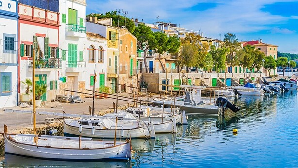 A waterfront with boats docked along the shore, buildings with balconies, and a clear sky. - Bella Maria Apartments & Pool Club (Felanitx)