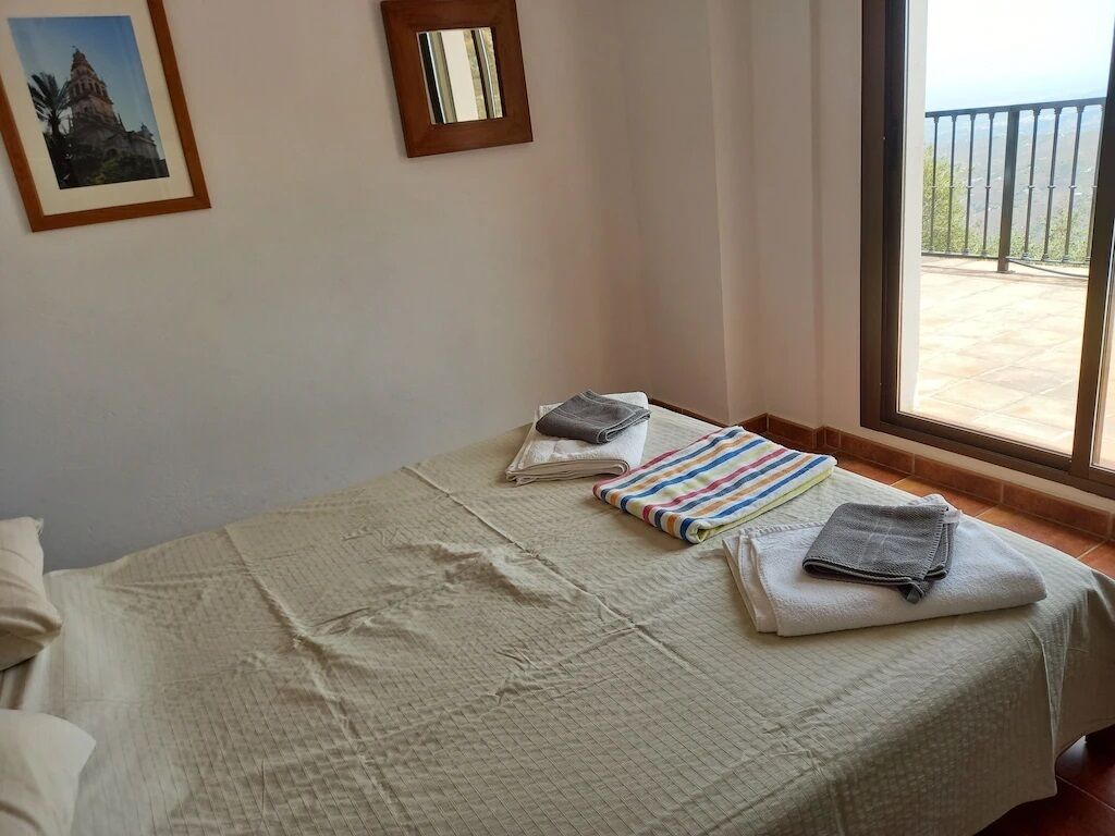 A room with a bed, a window with a balcony view, and a framed picture on the wall.