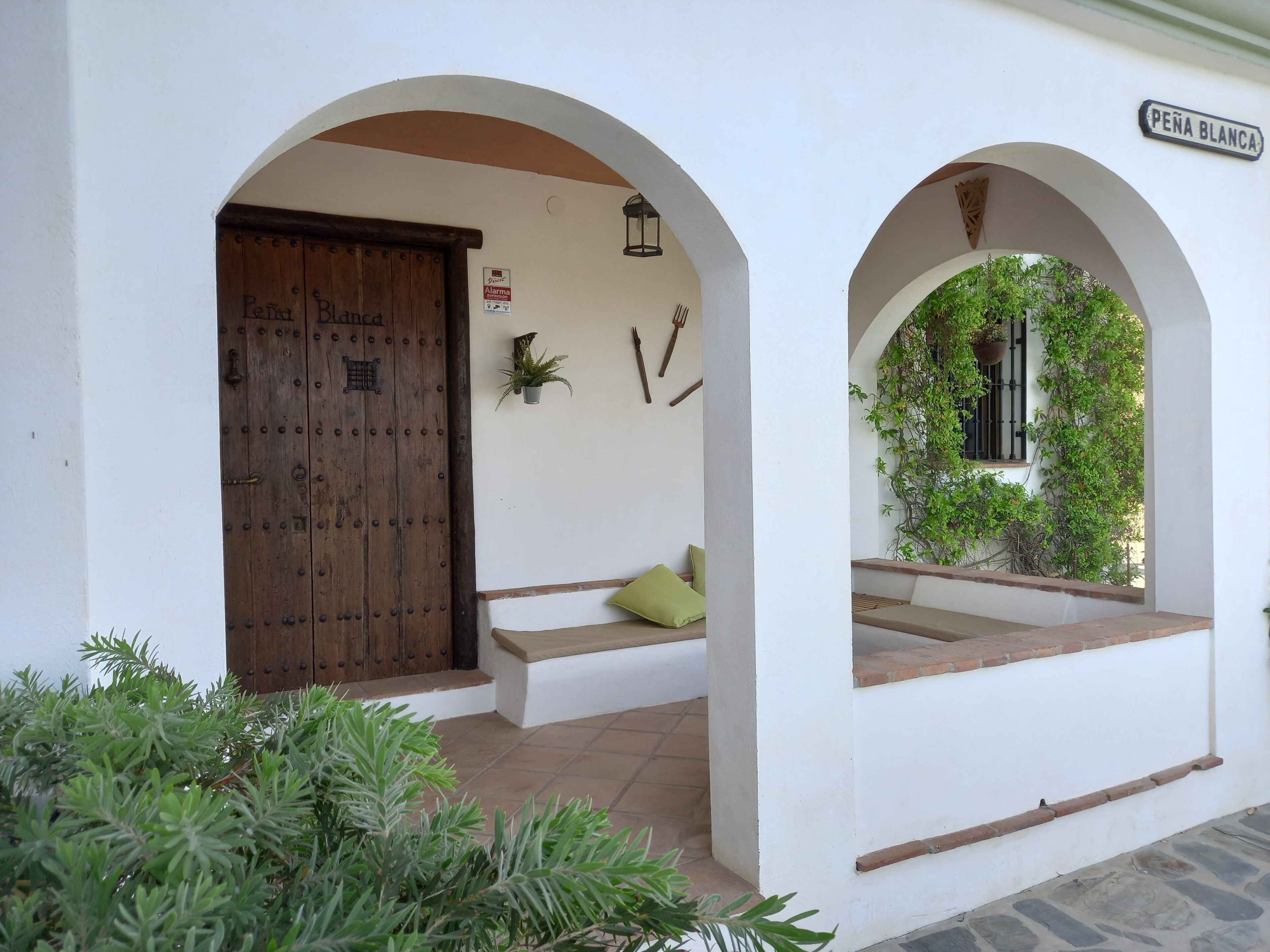 A white building with a wooden door labeled "Peña Blanca," a small bench, and a sign indicating a fire alarm.