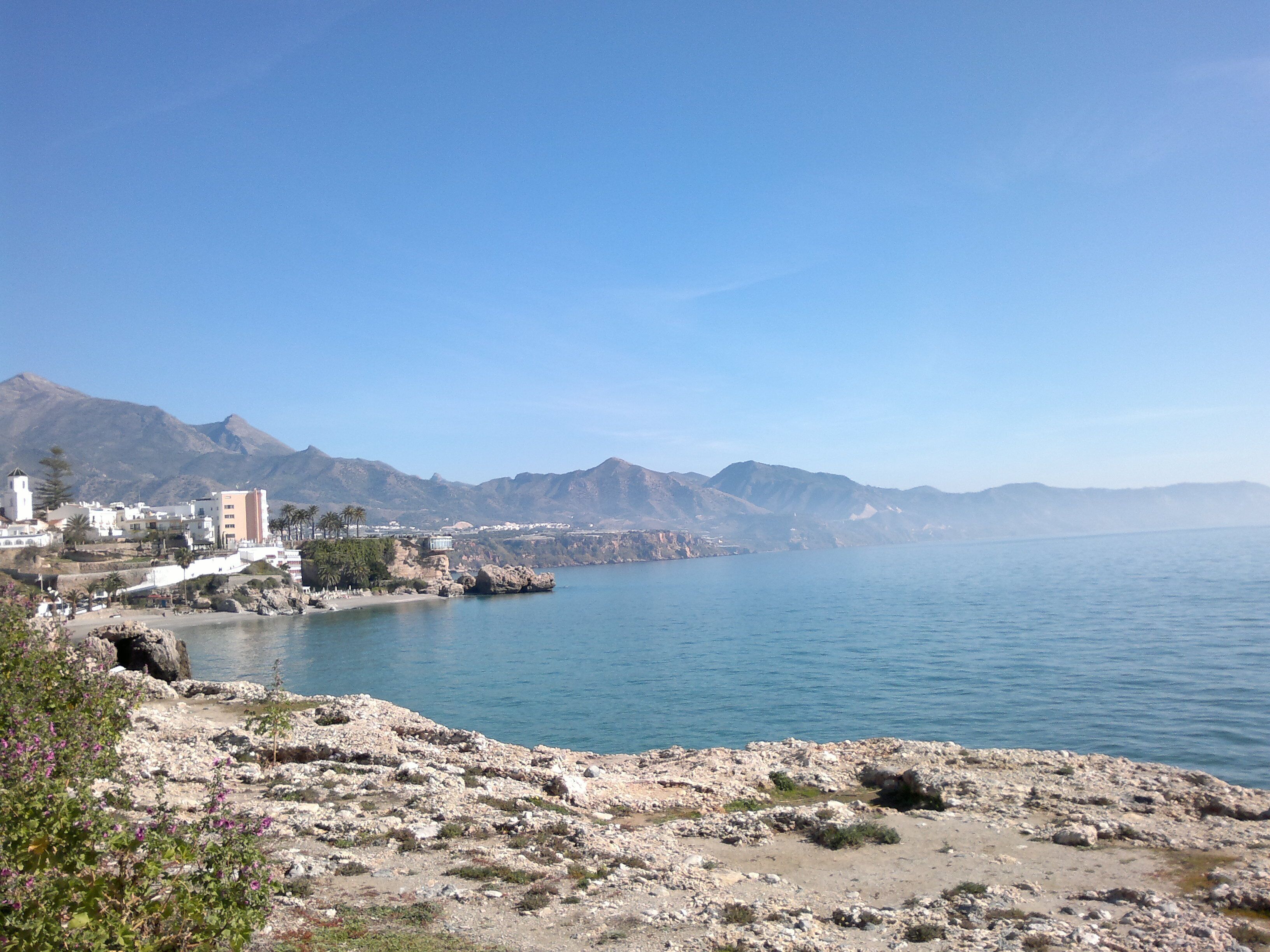 Eine Küstenstadt mit Gebäuden am Wasser, felsigem Gelände und Bergen im Hintergrund.