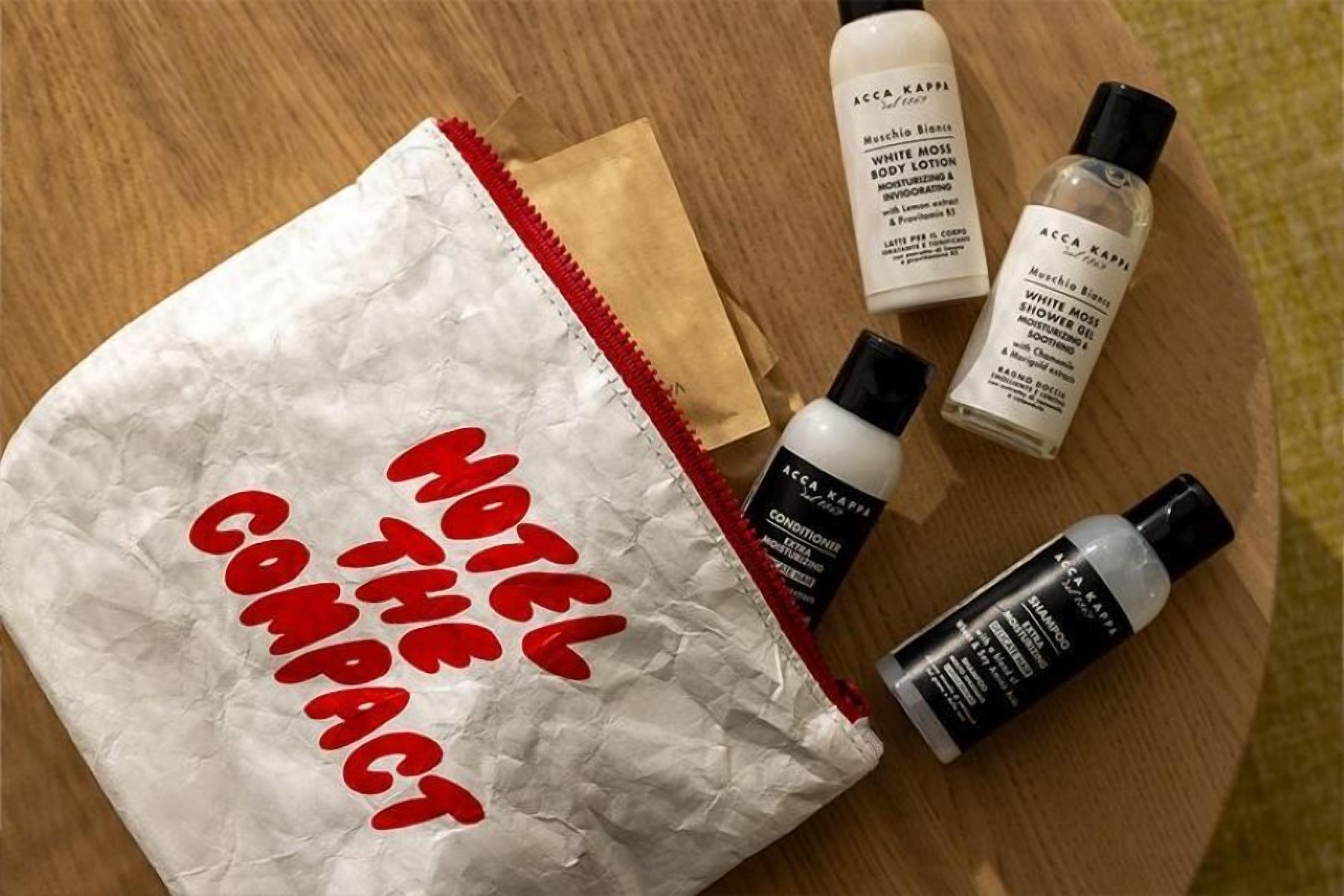 Ein zerknitterter Papierbeutel mit der Aufschrift 'HOTEL THE COMPACT' und drei Flaschen weiße Lotion.
