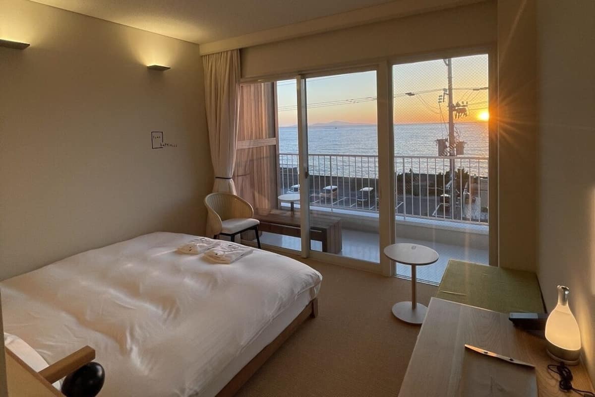 Habitación de hotel con cama, escritorio, silla y vistas al atardecer sobre el agua.