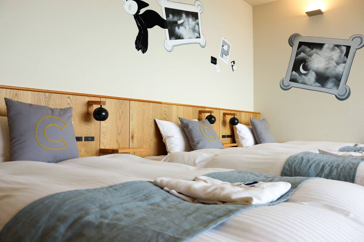 Habitación de hotel con una cama grande, varios almohadones, un cabecero de madera y decoraciones en las paredes, incluyendo cuadros y una lámpara de pared.
