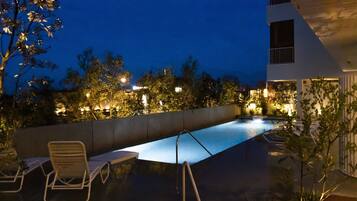 A rooftop pool area with lounge chairs and a view of the cityscape at night.