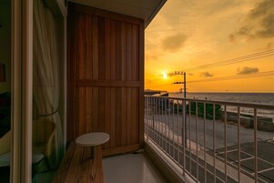 Un balcón con puerta de madera, una pequeña mesa redonda y vista al atardecer sobre el mar.