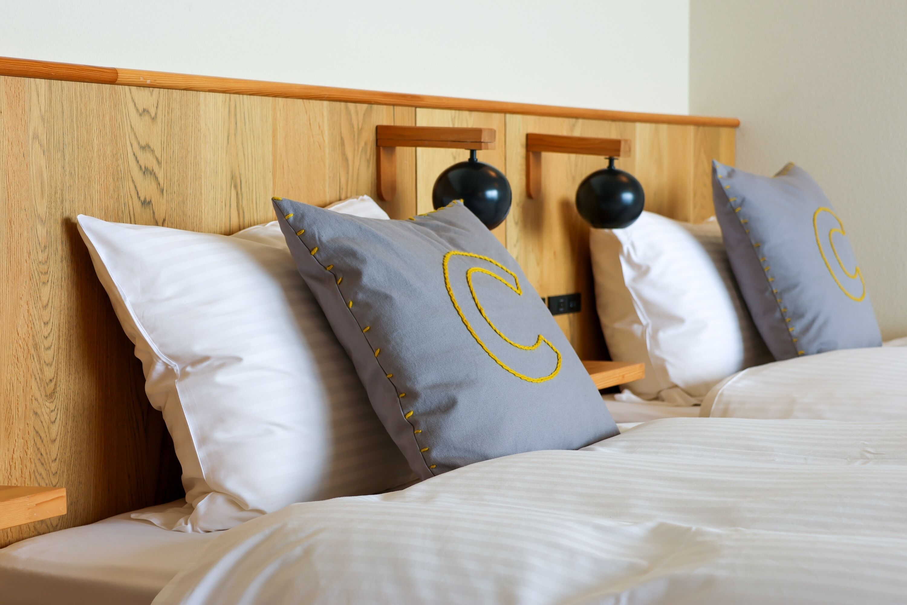 A neatly made bed with white linens and pillows featuring a large 'C' design.