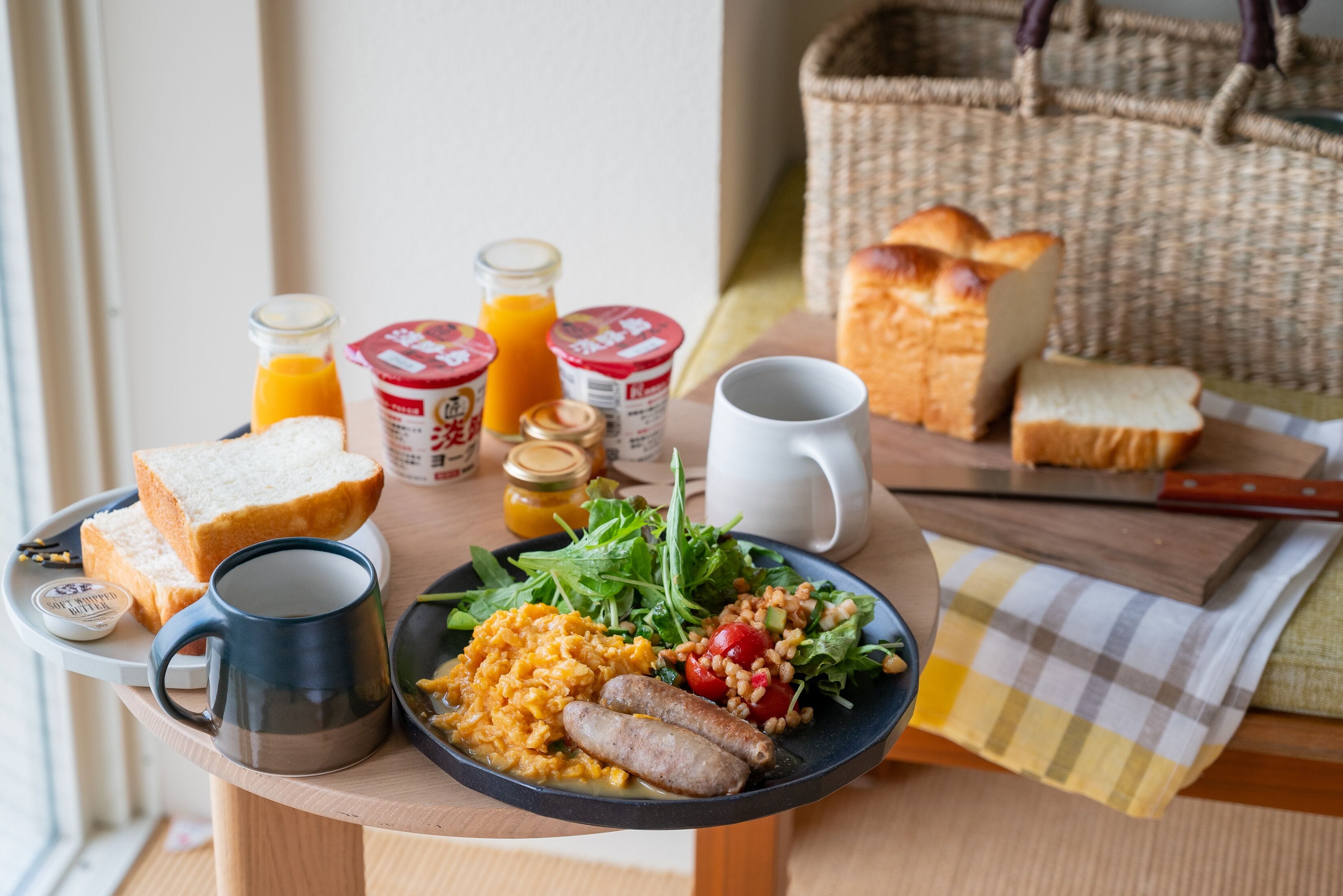 A breakfast table with bread, eggs, sausages, and a salad.
