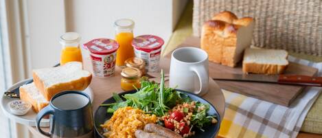 A breakfast table with bread, eggs, sausages, and a salad.