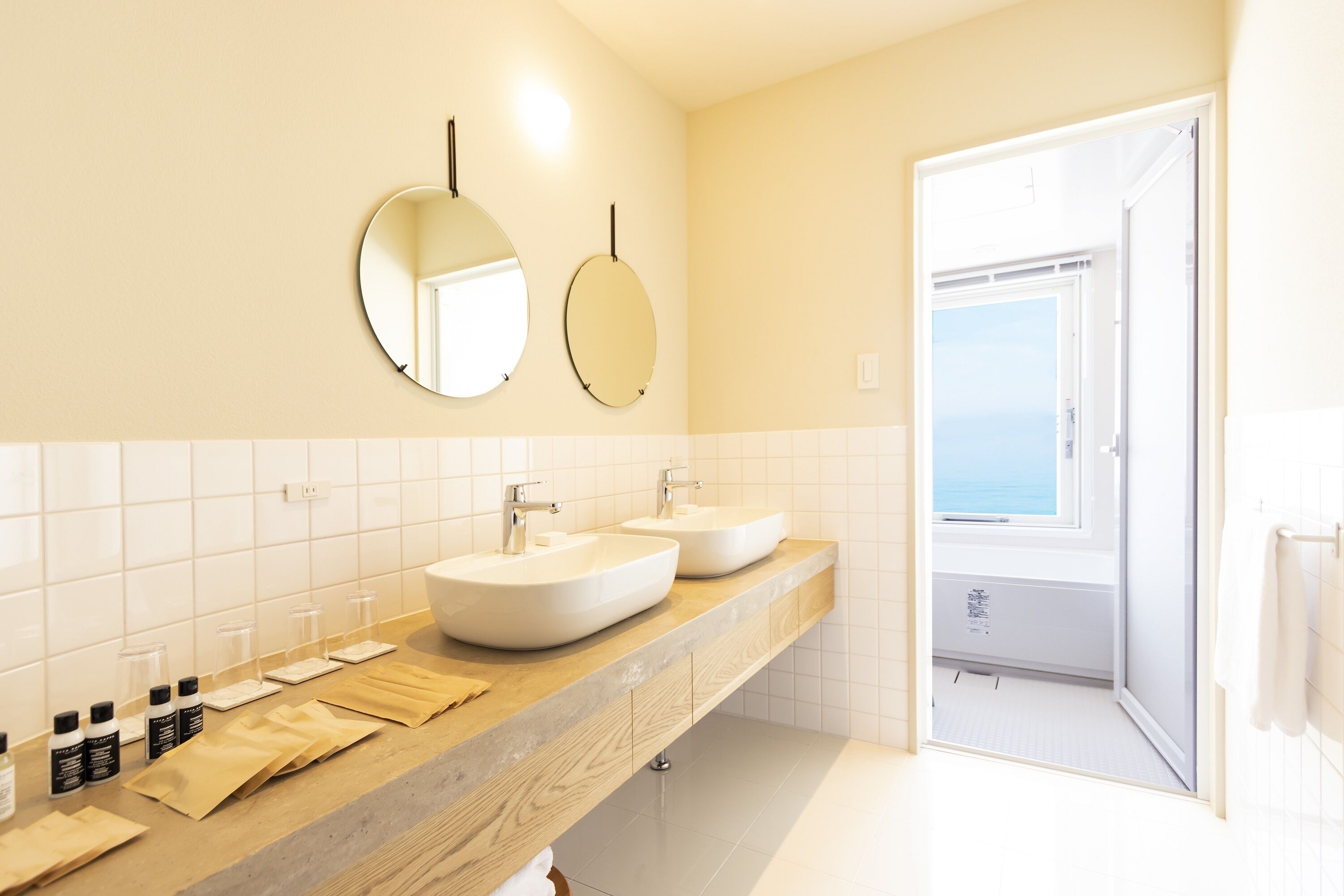 Une salle de bain avec deux lavabos, un miroir et une vue sur la mer, visible à travers une porte ouverte.