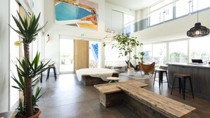A spacious, well-lit room with a large window, a wooden bench, a plant, and a painting on the wall. - KAMOME SLOW HOTEL THE COMPACT (Awaji)