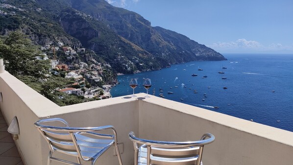A balcony with two chairs and two wine glasses, overlooking a coastal town with boats on the sea and mountains in the background. - House with a great terrace and spectacular views (Positano)
