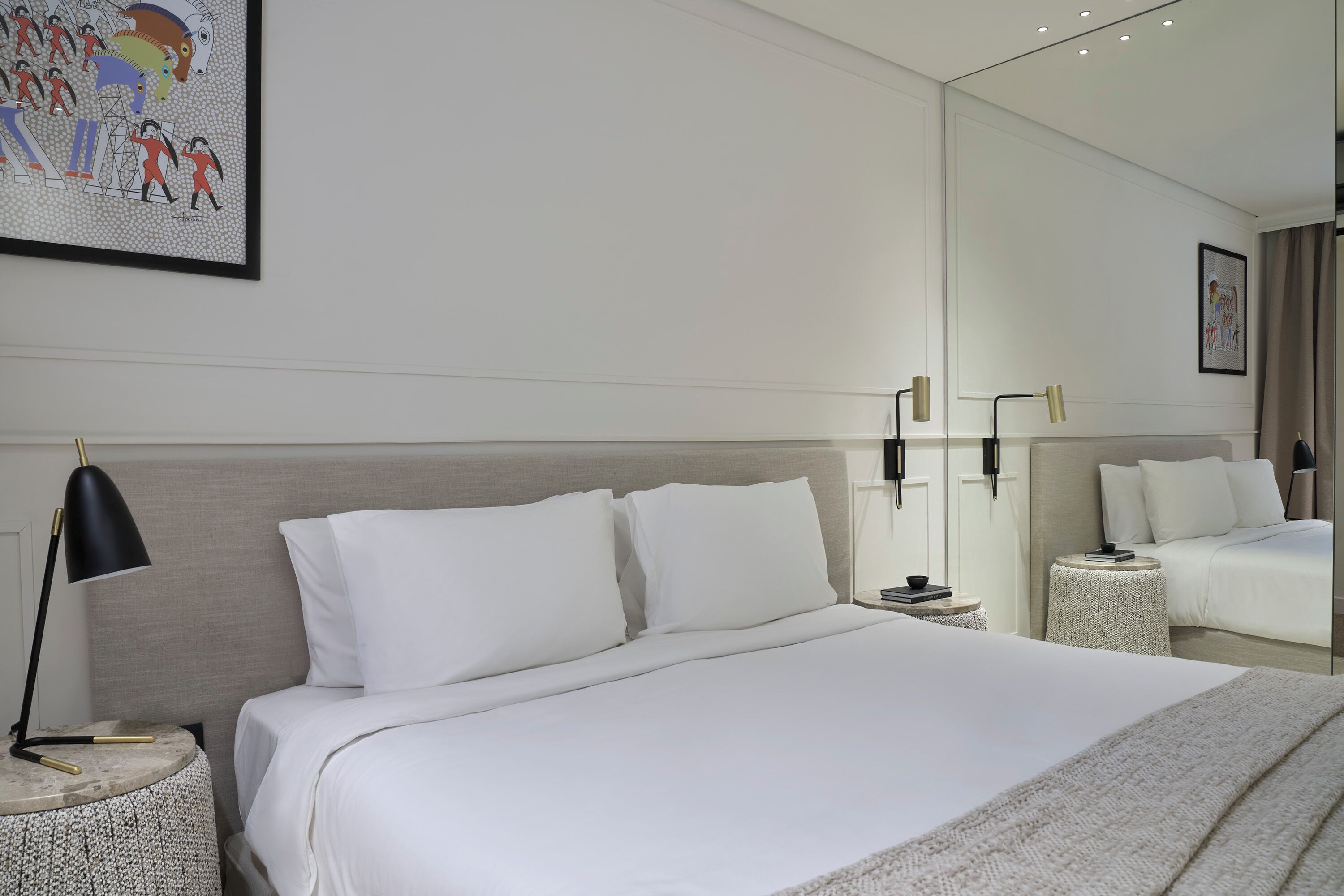Ein modernes Hotelzimmer mit einem großen Bett, Nachttischen, einem Spiegel und Bildern an der Wand.