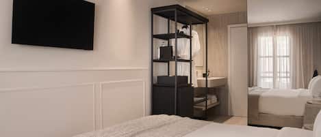 A modern hotel room with a large bed, a built-in TV, a wardrobe with shelves, and a bathroom with a mirror and curtains.