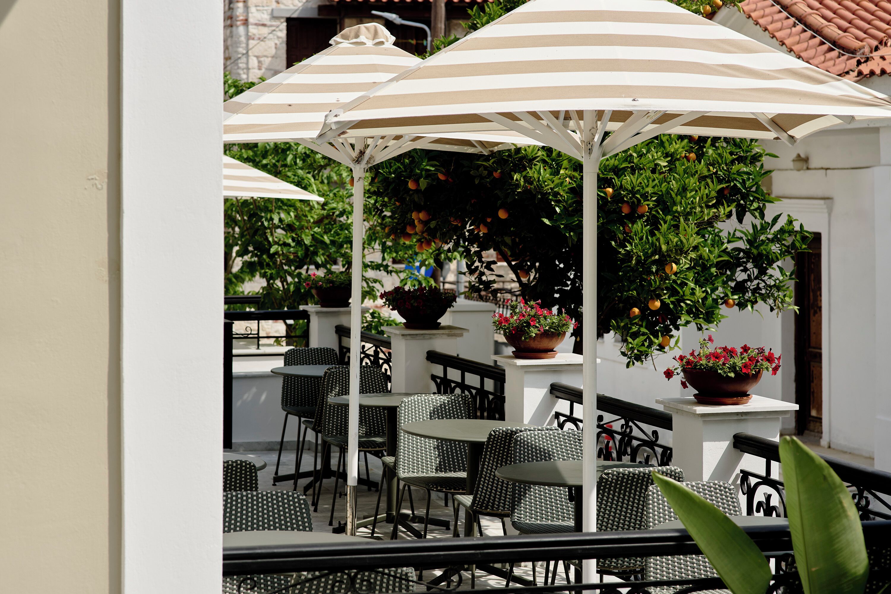 An outdoor seating area with tables and chairs, striped umbrellas, and potted plants.