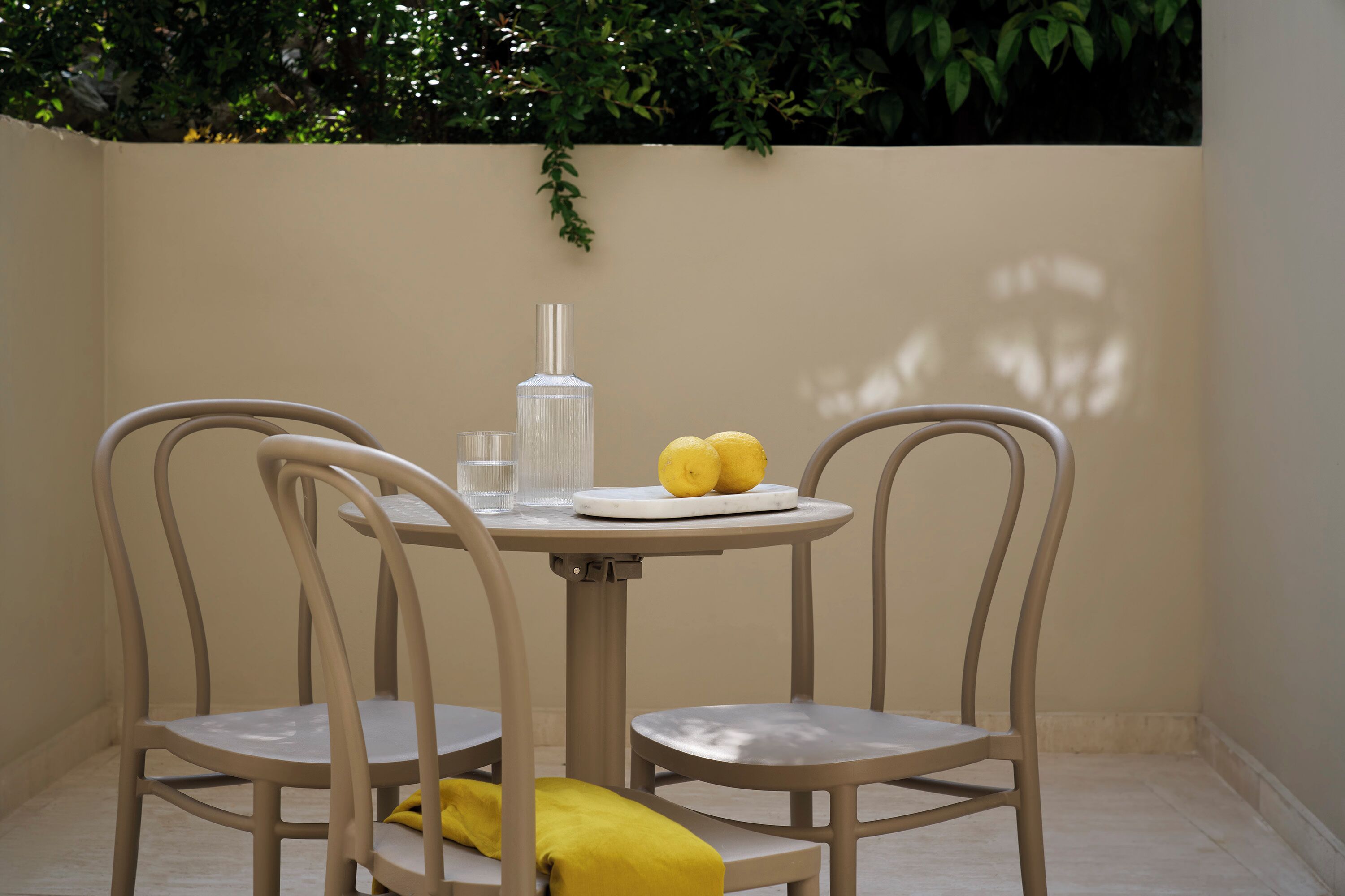 Un pequeño comedor con una mesa y dos sillas, una botella, dos limones y un vaso.