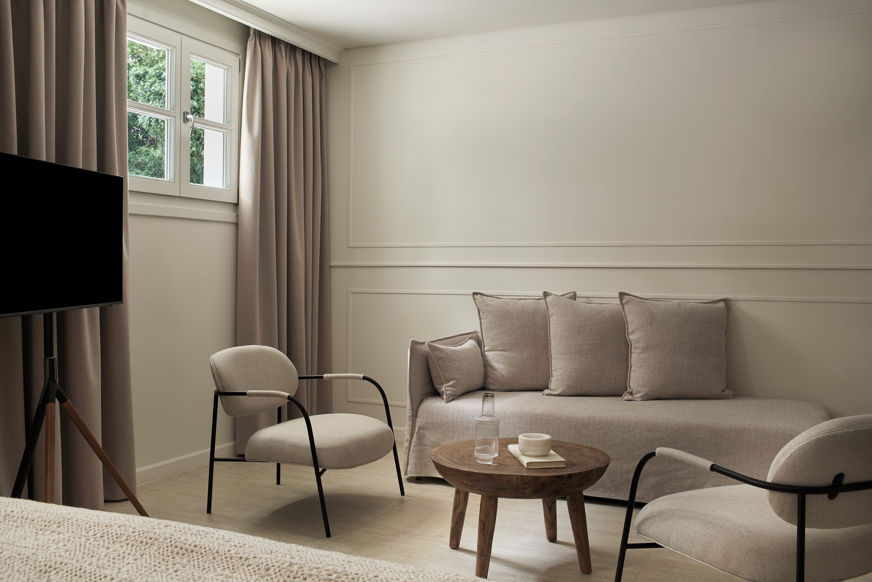 A modern, minimalist room with a sofa, two armchairs, a coffee table, and a television on a tripod stand.