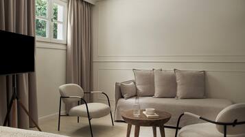A modern, minimalist room with a sofa, two armchairs, a coffee table, and a television on a tripod stand.