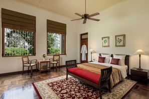 A bedroom with a bed, two chairs, a table, a ceiling fan, and two windows with blinds. - Jetwing Hoffmann Bungalow (Welimada)