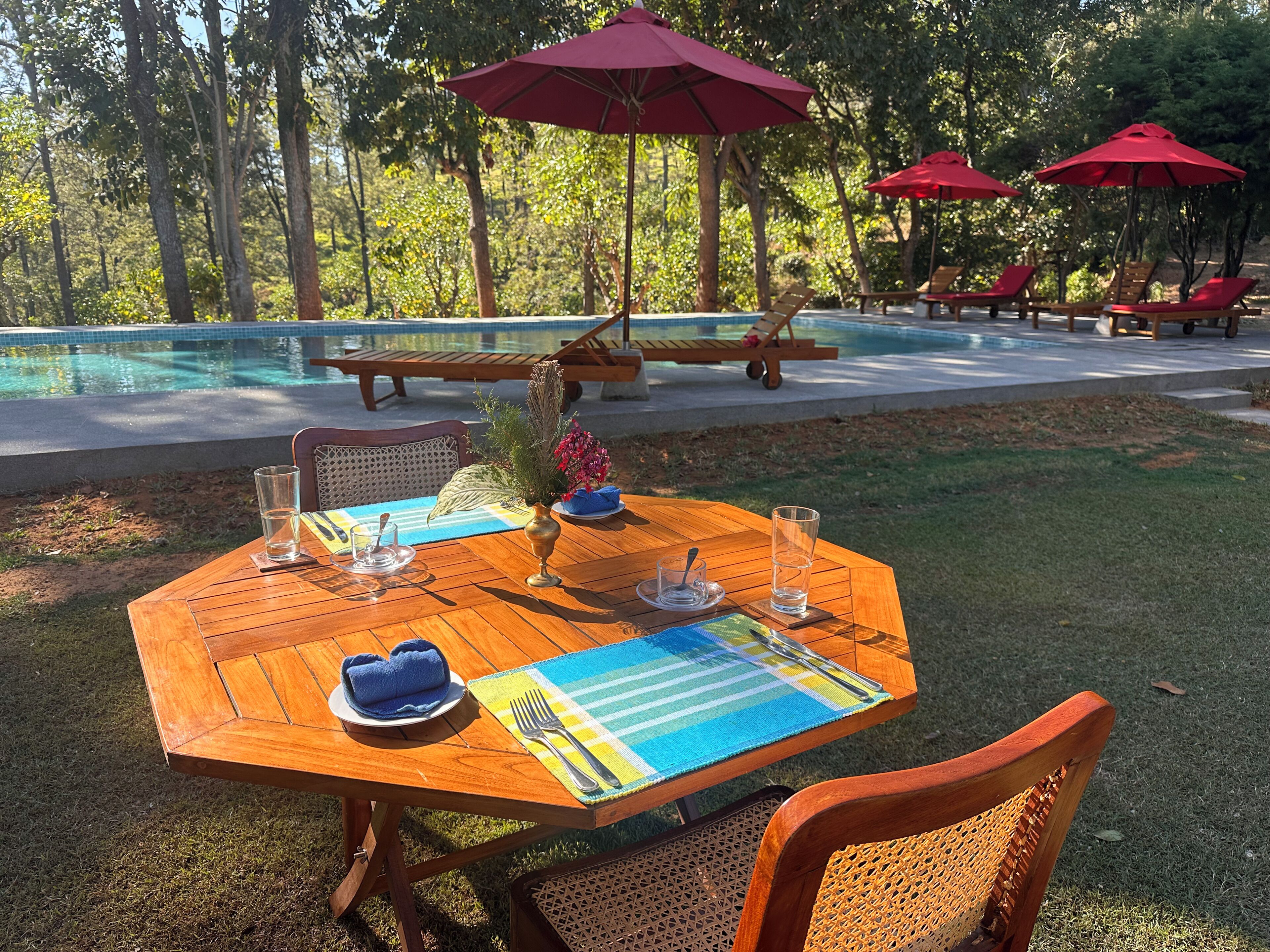 An outdoor dining area with a wooden table, chairs, and a pool in the background.