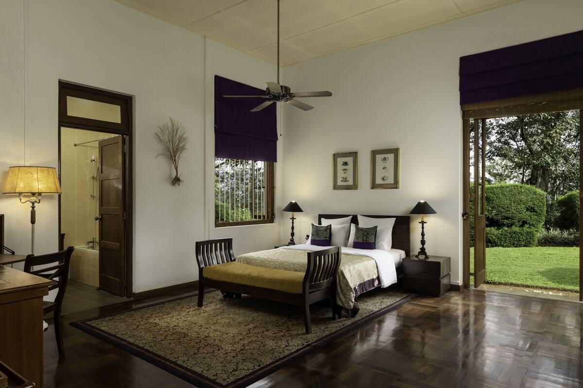 Un dormitorio con cama, mesitas de noche, escritorio, silla, ventilador de techo y vistas a un jardín.
