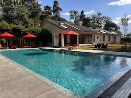 Una piscina con sillas de descanso y sombrillas, rodeada por un edificio con tejado de baldosas.