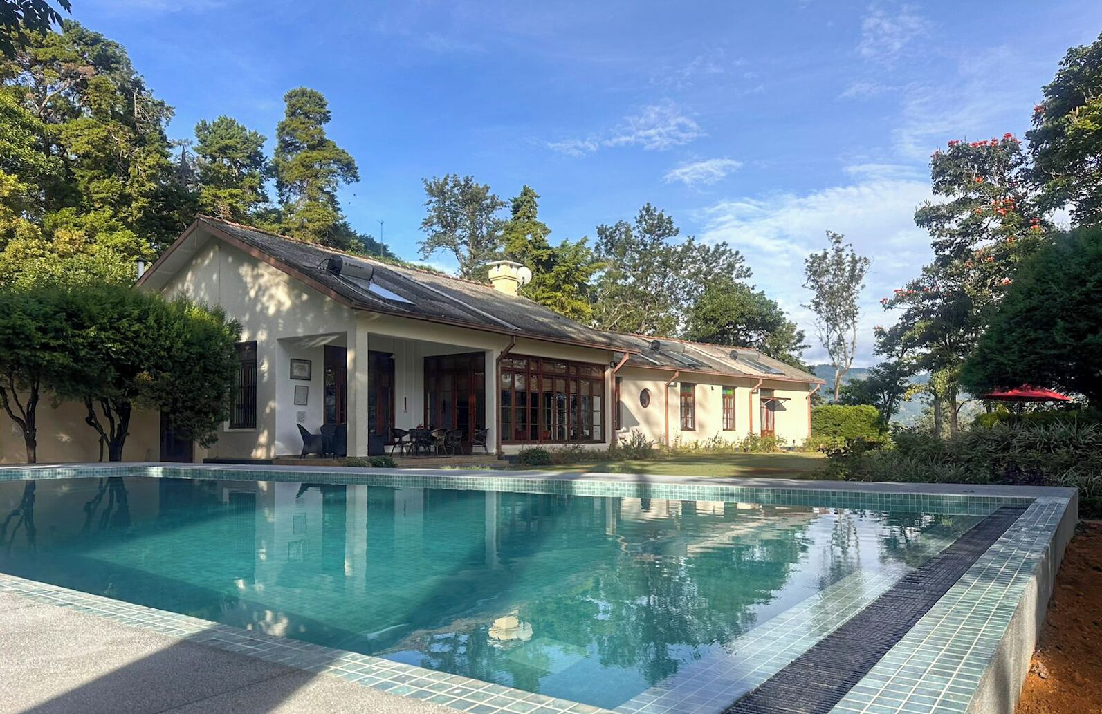 A house with a swimming pool, surrounded by trees and a clear sky.