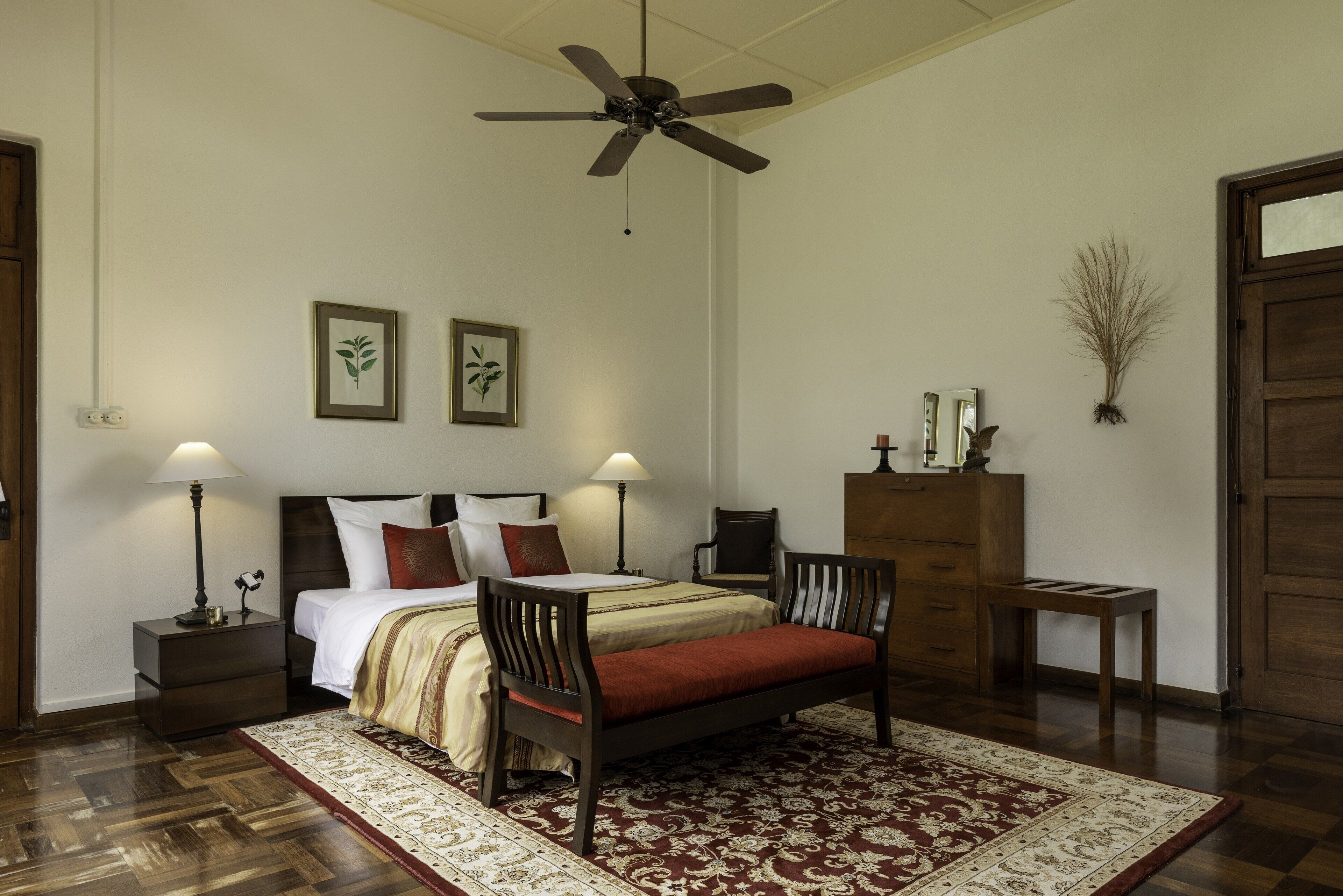 A bedroom with a bed, two chairs, a nightstand, a dresser, and a ceiling fan.