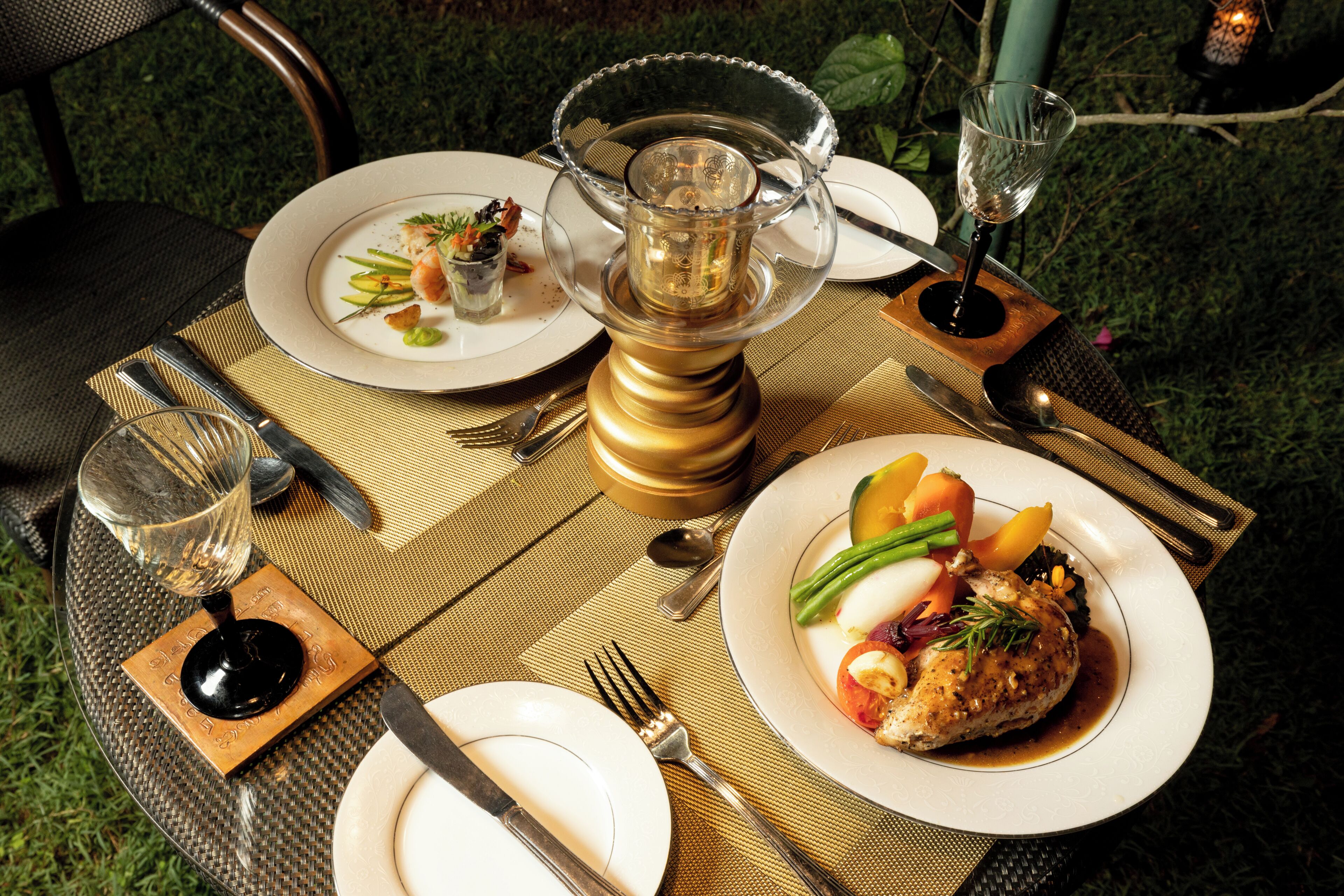 Une table dressée pour un repas, avec des assiettes remplies de nourriture, des couverts et un centre de table décoratif en verre.
