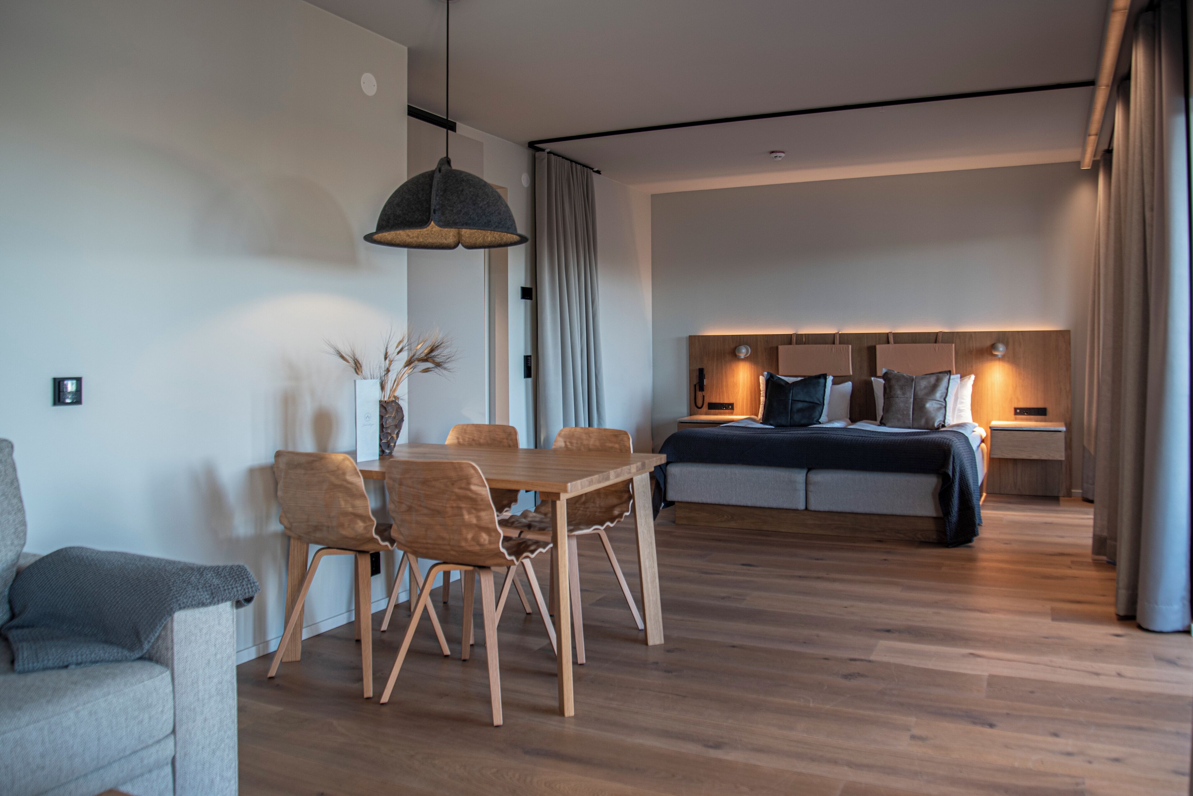 A modern living room with a wooden dining table, a sofa, and a bed with a headboard.