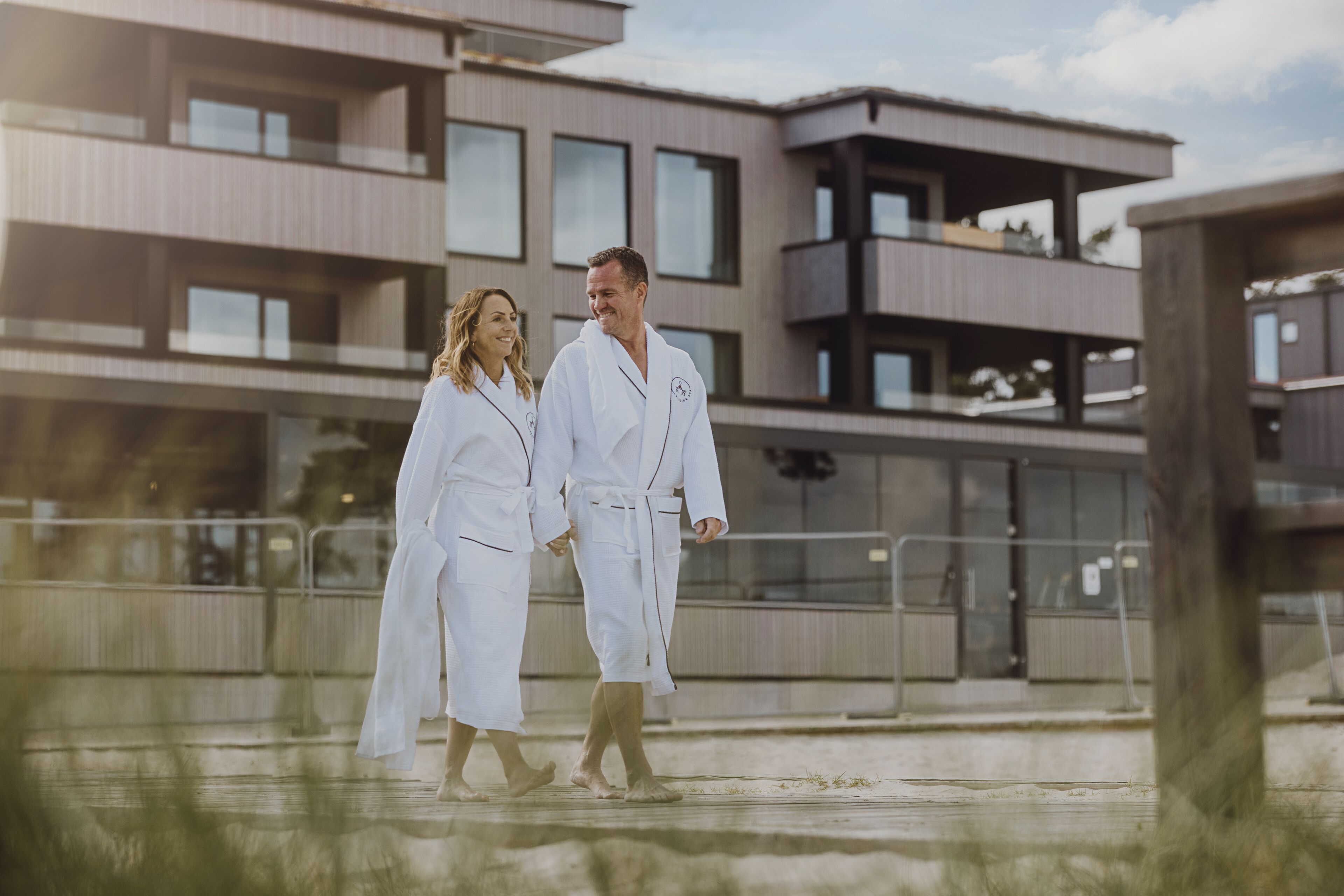 Two people in white robes walking on a balcony with a modern building in the background.