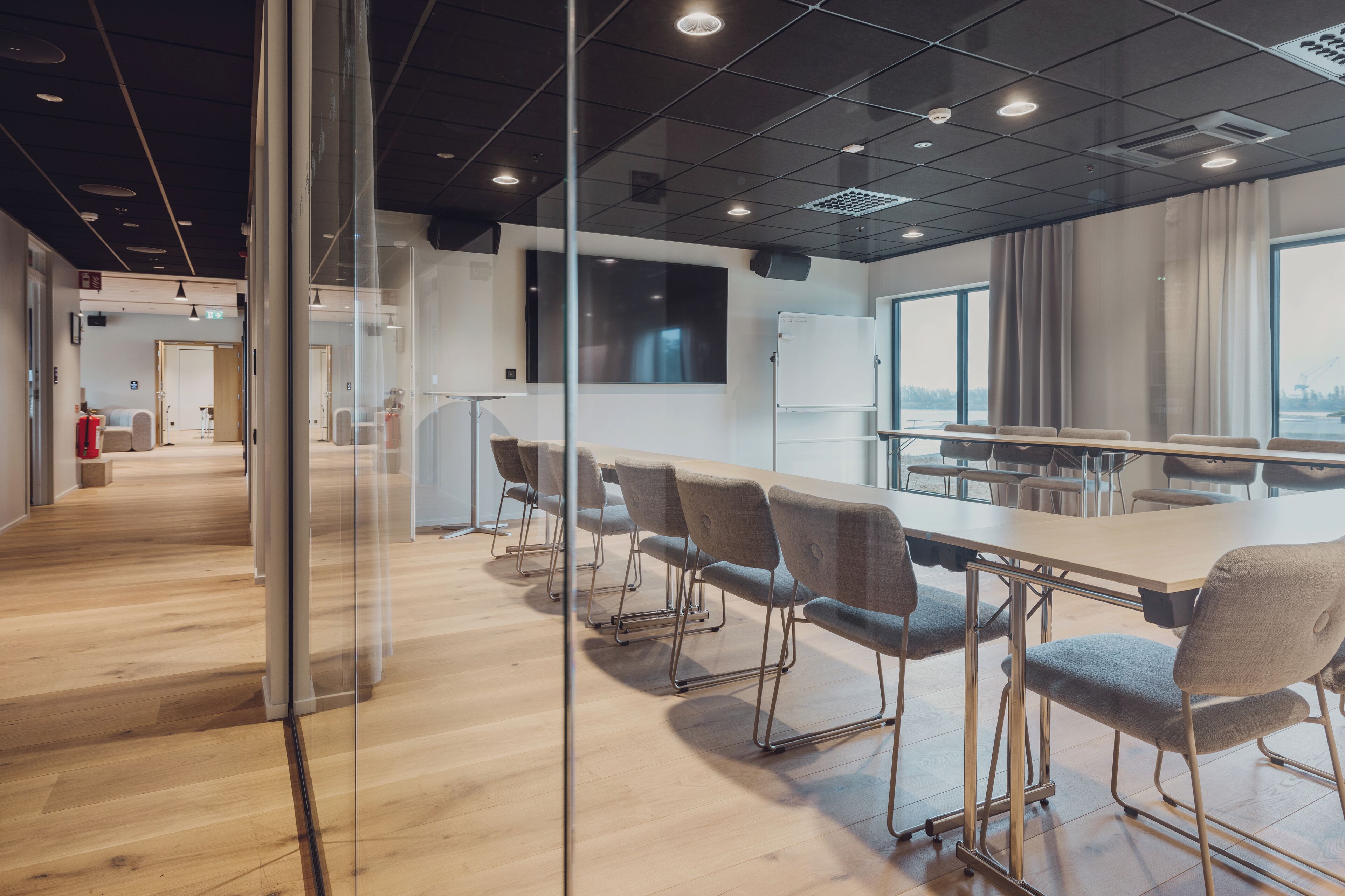 A modern conference room with a long table, chairs, and a large window with a view.