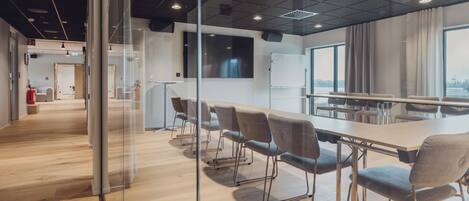 A modern conference room with a long table, chairs, and a large window with a view.