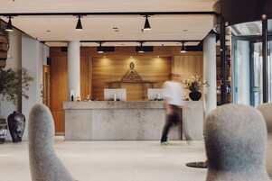 A modern reception area with a wooden reception desk, a large decorative piece above it, and a glass wall on the right.