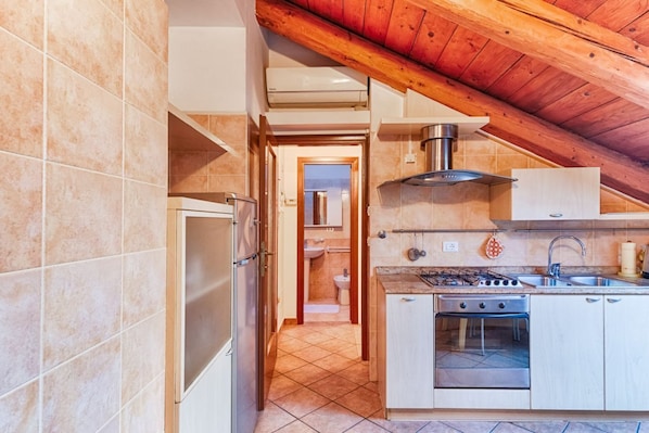 A kitchen with a stove, oven, and sink, a hallway leading to a bathroom, and a wooden ceiling.