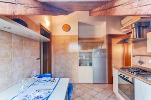 A compact kitchen with a dining table set for two, a refrigerator, a stove, and a clock on the wall.
