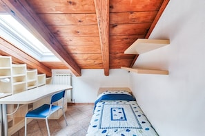 A small room with a sloped ceiling, a bed, a desk, and a chair. - GuestHost - Apartment located on the fifth floor of a building with a lift (there are 10 internal steps at the entrance to the apartment).In 45 sqm it comfortably accommodates 3 people, with a bedroom with two single beds and a sofa bed.Convenientlyt loc (Trieste)