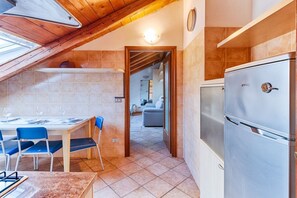 A kitchen with a modern stainless steel refrigerator, a dining area with blue chairs, and a wooden ceiling.