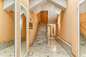 A hallway with a marble staircase, a mirrored wall, and a door on the left.