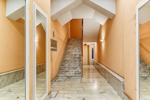 A hallway with a marble staircase, a mirrored wall, and a door on the left.