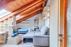 A loft-style bedroom with a sloped ceiling, built-in shelving, a bed, a sofa, and a desk with a computer.