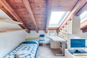 A small, cozy room with a sloped ceiling, a bed with a patterned bedspread, a desk with a chair, and a computer setup.