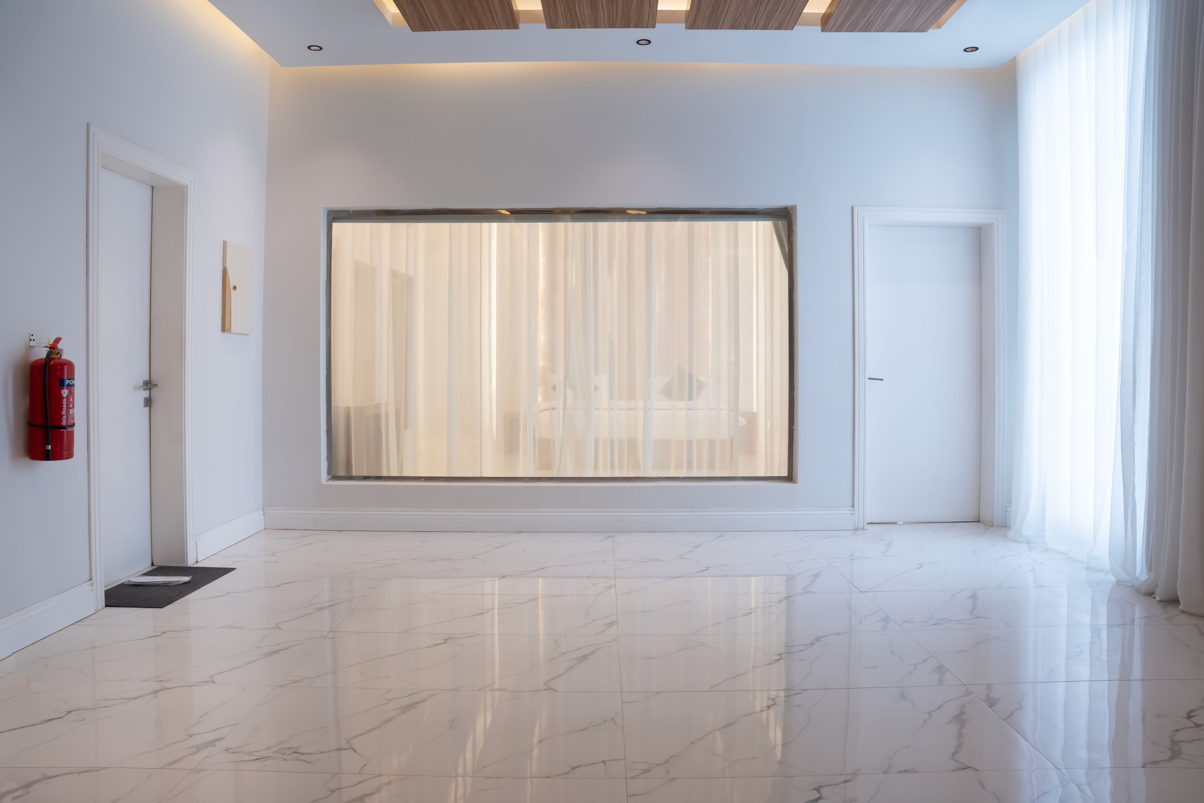 A spacious room with a large sliding glass door, a fire extinguisher on the wall, and a clean, polished marble floor.