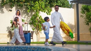 Une famille se promène près d’une piscine : un enfant tient un ballon de football et un autre, une planche de surf.