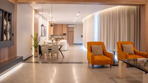 Un salon moderne avec deux fauteuils orange, une table basse en verre et un coin repas comprenant une table et des chaises blanches.