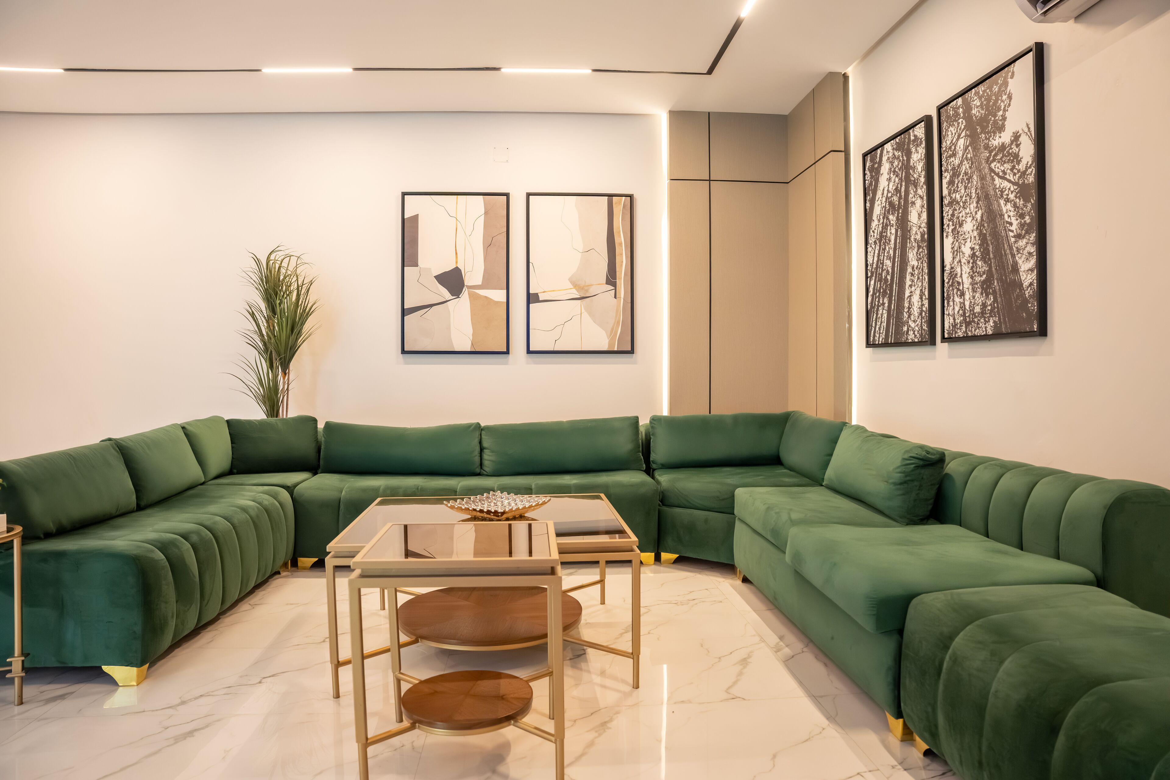 Un salon moderne avec un canapé d’angle vert, une table basse en verre et deux tableaux abstraits accrochés au mur.