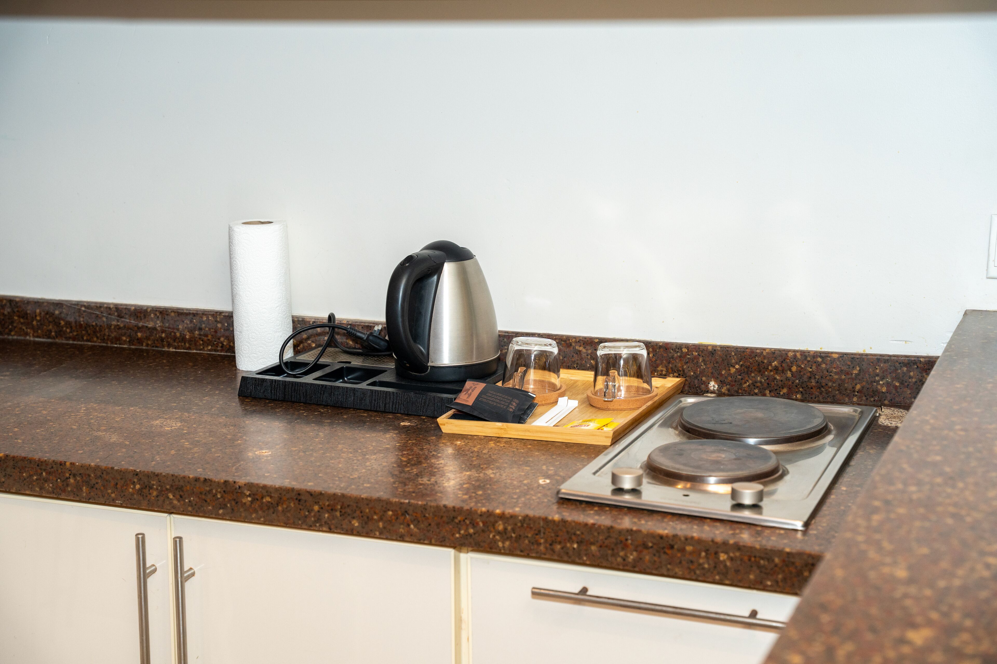 A kitchen counter with a kettle, a roll of paper towels, and two glasses on a tray.